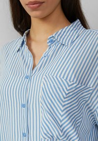 Lichtblauw en wit gestreept shirt met een button-down kraag, voorzien van blauwe knopen en een linkerk borstzak met een diagonaal streeppatroon.