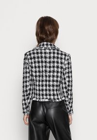 Svart och vit rutig skräddarsydd jacka med brättad krage, strukturerad form och textilstruktur, kombinerad med svarta läderbyxor.