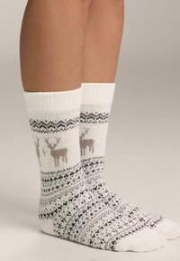 Kremowe, sięgające do kolan skarpety z dzianiny z wzorem renifera w beżowym, szarym i czarnym kolorze, ozdobione dekoracyjną bordiurą i o miękkiej fakturze.