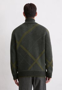 Knitted green sweater with a textured finish, featuring diagonal yellow lines and a high collar. Visible seam details at the cuffs and hem.