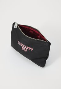 Poche en nylon noir avec doublure matelassée bordeaux, dotée d'une fermeture éclair argentée et du logo "CARHARTT WIP" en lettres rouges.