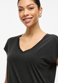 Črna majica s kratkimi rokavi in V-izrezom, izdelana iz gladkega blaga. Ponuja sproščen kroj in subtilno teksturo, idealna za vsakdanjo uporabo.