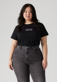 Black cotton t-shirt with short sleeves and logo "LEVI'S" printed in white. Paired with high-waisted dark gray jeans featuring classic pockets.