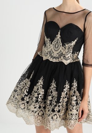 Schwarzes Kleid mit transparenten Ärmeln, herzförmigem Ausschnitt und aufwändiger goldener Blumenstickerei am Oberteil und Saum des Rocks.