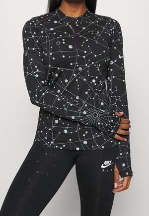 Frau trägt schwarzen Langarm-Top mit weißen Sternbildmustern und schwarze Nike-Leggings mit weißem Nike Air-Logo am linken Oberschenkel.
