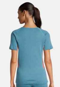 Top corto blu con maniche raglan. I pannelli laterali di un leggero corallo aggiungono contrasto. Texture morbida e vestibilità relax per il massimo comfort.