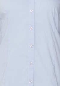 Light blue button-up shirt made of smooth fabric, featuring a front placket with buttons and long sleeves. Simple design with no patterns.