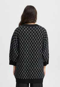 Pull en tricot noir avec un motif en losanges blanc et bleu clair, présentant une coupe ample, des épaules tombantes et des poignets côtelés.