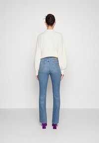 Bílý pletený svetr s vysokým límcem, doplněný světle modrými zvonovými džíny. Výrazné fialové boty na podpatku a detaily se třepením na lemu.