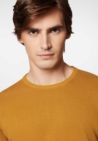 Musztardowy, prążkowany sweter z okrągłym dekoltem. Gładka faktura w okolicy klatki piersiowej, dopasowany krój z krótkimi rękawami.