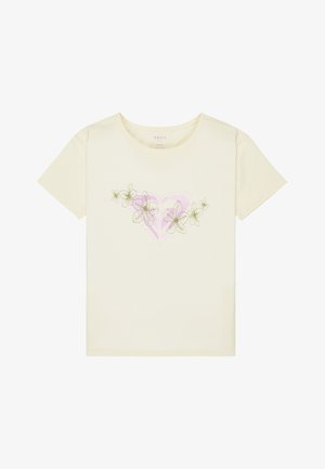 Fille souriante debout, les mains sur les hanches, portant un t-shirt blanc avec un cœur rose et des fleurs, un short rayé, des chaussettes blanches et des chaussures marron sans lacets.