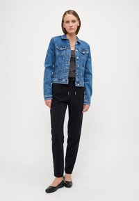 Denimjakke i lys blå, med knapper og frontlommer; slanke svarte bukser med elastisk midje; svarte flate sko. Minimalistisk design, glatt tekstur.