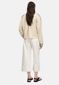 Beige leather jacket with a cropped design and pronounced shoulder seams, paired with wide white trousers and black strappy sandals.
