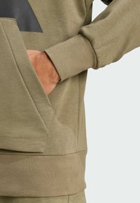 Olivgrön sweatshirt med känguruficka, ribbad mudd och en texturerad triangeldetalj på framsidan för extra stil.