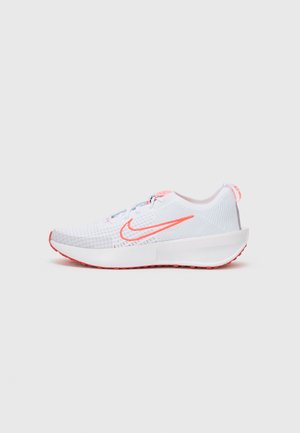 Hvit sportssko med teksturert mesh-overdel, rosa detaljer og en polstret såle. Har en fremtredende oransje Nike-logo på siden.
