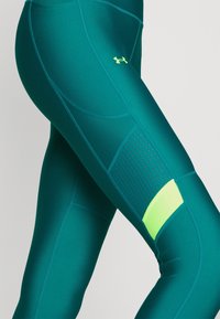 Leggings sportivi color teal con una texture liscia, caratterizzati da un pannello forato e un accento in verde neon. Il design sagomato migliora la vestibilità.