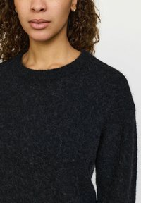 Must terivaade, ümar kaelus, pehme ja tekstuuriga viimistlusega ning laia lõikega mustad kootud sviitrid. Ei mingeid nähtavaid mustreid ega metallosi.