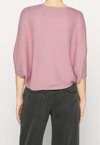 Top en maille mauve à coupe ample avec une texture côtelée et des manches larges, associé à un jean taille haute gris foncé avec des poches arrière.