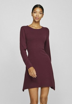 Abito lungo bordeaux a maniche lunghe con scollo rotondo, corpino aderente e orlo asimmetrico. Realizzato in un tessuto a maglia testurizzato.