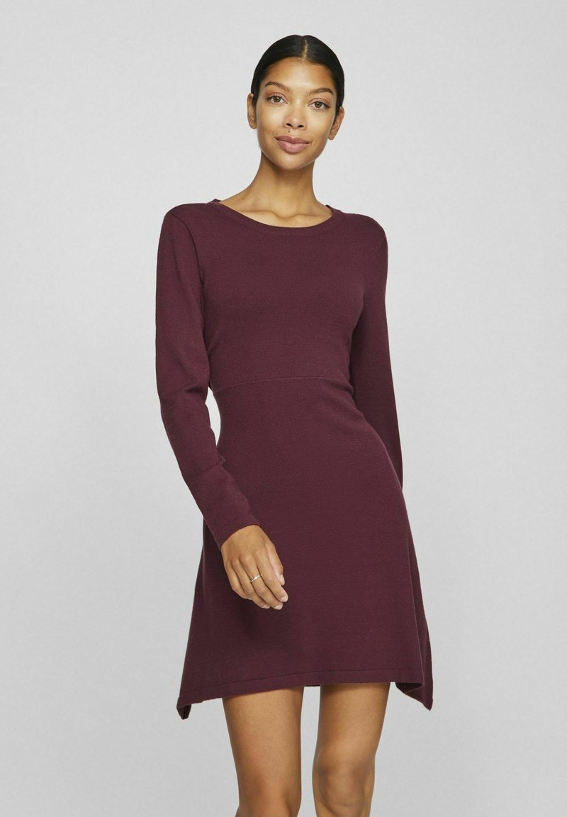 Abito lungo bordeaux a maniche lunghe con scollo rotondo, corpino aderente e orlo asimmetrico. Realizzato in un tessuto a maglia testurizzato.