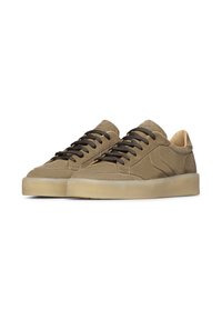 Un paio di sneakers in suede beige con lacci marroni scuri e spesse suole in gomma trasparente su uno sfondo bianco.