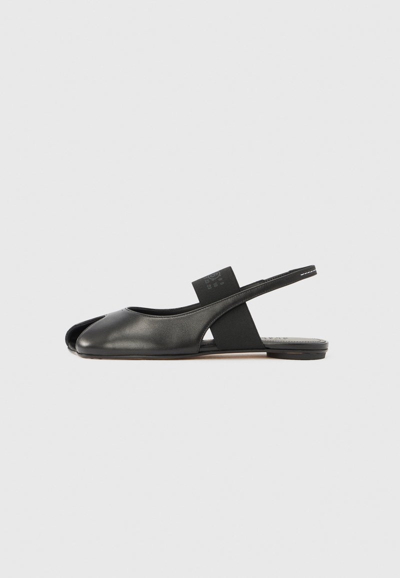 Melns ādas atvērtā purngala zemais apavu pēdas ar elastīgu siksnu pār pēdas izliekumu, redzams profilā uz vienkārša baltā fona.