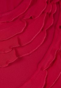Red fabric featuring layered, wavy ruffles with a sheer texture. The edges are stitched with a contrasting thread for added detail.