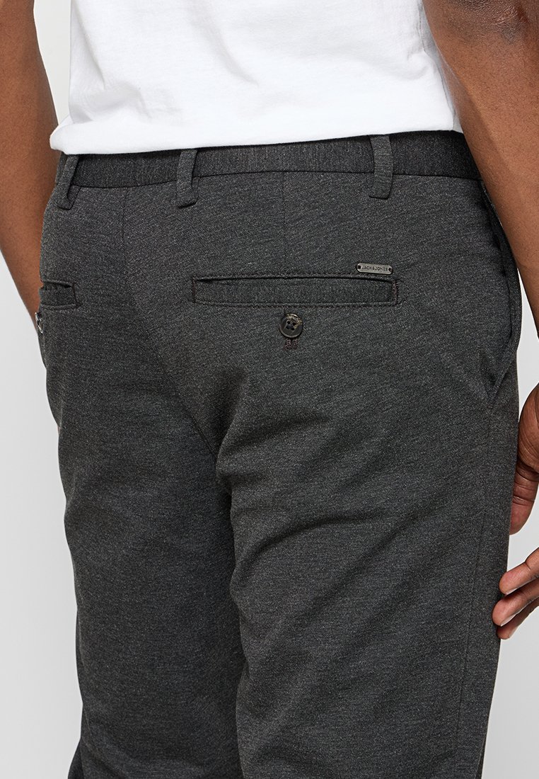 Ciemnoszare spodnie uszyte z fakturowanej tkaniny, charakteryzujące się prostym designem, dwiema tylnymi kieszeniami z guzikami oraz akcentem w postaci logo.