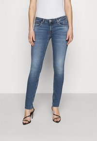 Jeans skinny de denim azul claro, con una cintura de altura media, dobladillo deshilachado y diseño clásico de cinco bolsillos. Combinados con tacones negros con tiras.