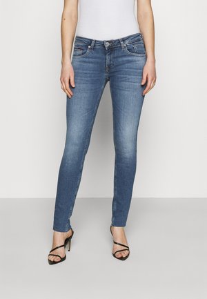 Jeans skinny de denim azul claro, con una cintura de altura media, dobladillo deshilachado y diseño clásico de cinco bolsillos. Combinados con tacones negros con tiras.