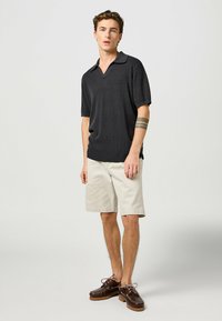 Kortærmet, mørkegrå polo-shirt med V-halsdesign, parret med beige shorts og brune sko. Glat tekstur, afslappet pasform.