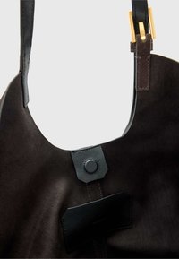 Bolsa de mão em camurça preta com forma arredondada, realçada por uma alça de couro e fecho de metal. Apresenta uma textura suave e um design minimalista.