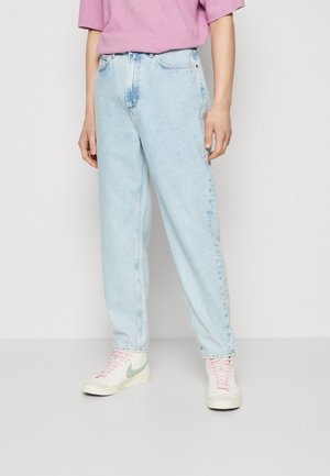 Persona vistiendo jeans de cintura alta color azul claro, camiseta rosa de manga corta y zapatillas blancas con cordones rosas y el logo de Nike en verde.