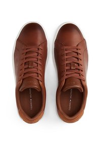 Braune Leder-Sneaker mit glatter Textur, silbernen Ösen, weißen Gummisohlen und Logodetail auf der Innensohle. Klassisches sportliches Design.