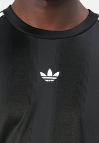 Μαύρο αθλητικό μπλουζάκι με κάθετες ρίγες, υφασμάτινη υφή και λευκό λογότυπο Adidas στο στήθος. Στρογγυλεμένος γιακάς με διακριτικές λεπτομέρειες.