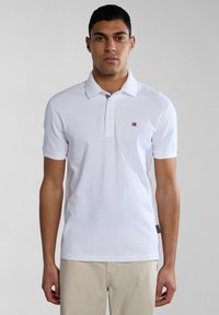 Polo bianco con colletto classico, maniche corte e un piccolo emblema a forma di bandiera sul lato sinistro del petto. Realizzato in morbido tessuto di cotone.
