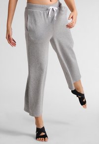 Szare, lekkie, skrócone spodnie dresowe z elastycznym pasem, sznurkiem do regulacji, bocznymi kieszeniami i prostą nogawką, zestawione z czarnym obuwiem z odkrytymi palcami.