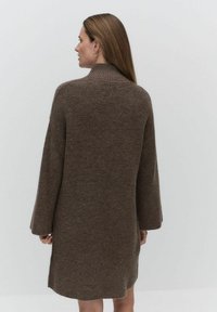 Brun stickad klänning med hög krage, långa ärmar och avslappnad passform, med en mjuk textur och en lätt rundad fåll.