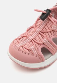Rozā acs sporta apavi ar mīkstu gumijas zoli, elastīgām auklām un atvērtām malām ventilācijai, ar kontrastējošiem baltiem šuvumiem.