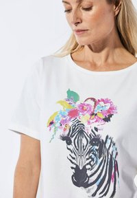 Witte t-shirt met korte mouwen met een zebraafbeelding versierd met kleurrijke bloemen, met zwart-witte strepen en levendige bloemenaccenten.