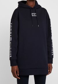 Merinavy hooded sweatshirt with front pocket, logo accents on the chest and sleeves, and ribbed cuffs at the sleeves and hem.