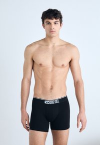 Boxer-briefs noirs avec un logo "DIESEL" blanc sur la taille. Le tissu semble lisse et élastique, épousant étroitement le corps.