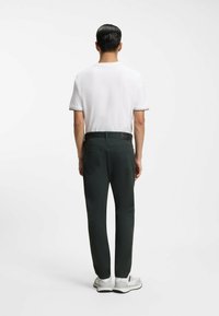 Polo bianca a maniche corte con rifiniture nere e beige, abbinata a pantaloni verde scuro. Scarpe bianche con dettagli grigi e suole nere.