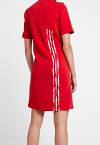 Kort röd klänning med korta ärmar, med en sidodesign av tre vita ränder med ett strukturerat mönster längs ryggen.