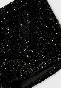 Tessuto nero con paillettes, caratterizzato da un motivo a onde testurizzato e impreziosito da paillettes argentate lucide. Fodera liscia lungo il bordo.