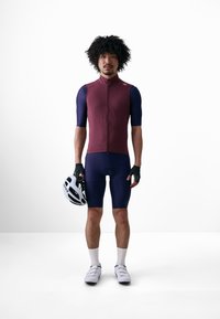 Tenue de cyclisme à manches courtes avec un haut bordeaux et un short bleu marine. Les accessoires comprennent un casque blanc et des gants noirs ; design ajusté.
