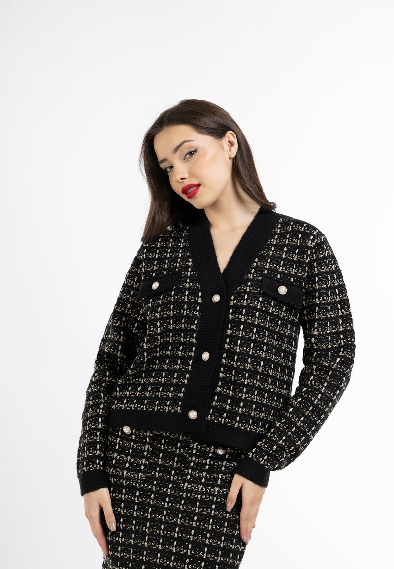 Schwarze und cremefarbene Textur-Strickjacke mit V-Ausschnitt, zwei Taschenklappen und perlenartigen Knöpfen an der Vorderseite und den Bündchen. Sichtbare Strickdetails im Stoff.
