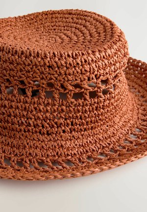 Braided straw hat in a terracotta color with a rounded crown and wide, floppy brim. Features open weave patterns around the sides.