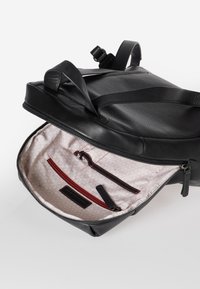 Zaino in pelle nera con esterno testurizzato, interno crema con motivo geometrico e molteplici tasche tra cui un compartimento con cerniera.