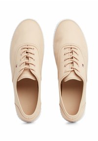 Beige kangaskengät valkoisilla kumipohjilla, joissa on nauhakiinnitys ja hillitty logoyksityiskohta sivulla. Kengissä on sileä pinta.